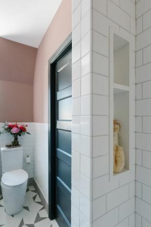 mur peint en rose, carrelage métro blanc, toilettes blanches, carreaux géométriques blancs et gris, étagères intégrées