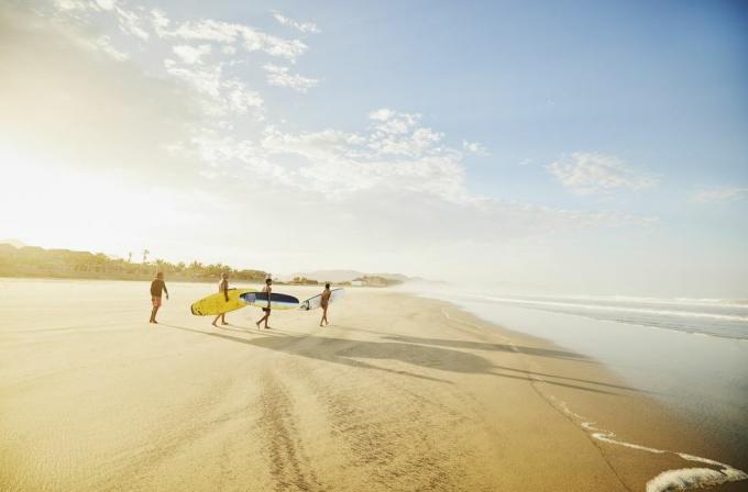 Plan extrêmement large d'une famille transportant des planches de surf sur une plage tropicale tout en prenant des cours de surf pendant les vacances