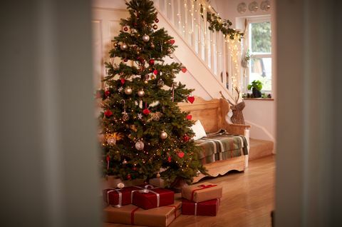 Couloir de la maison décorée pour Noël avec arbre et cadeaux vu à travers la porte ouverte