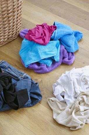 Des vêtements sales séparés en tas sur un plancher en bois à côté du panier à linge