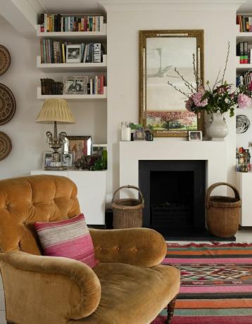 Fauteuil boutonné marron de George Smith dans un salon blanc avec tapis marocain et cheminée, appartement londonien de l'architecte d'intérieur Sarah Vanrenen