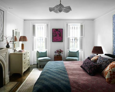 chambre à coucher, chaises bleues, linge de lit rouge, tapis vert, coussins décoratifs, cheminée, plafonnier blanc