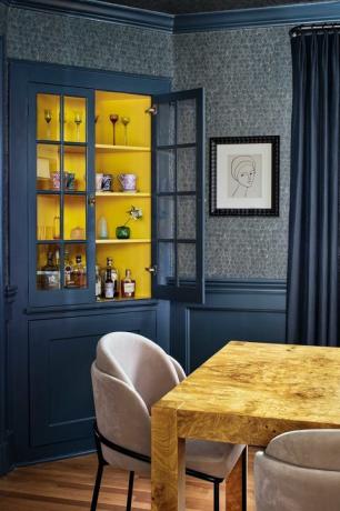 salle à manger avec murs peints en bleu et revêtement mural bleu foncé, meuble bar avec alcool, chaise de salle à manger en bois avec chaises de salle à manger en velours rose