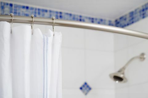 Détail rideau de douche et pomme de douche en douche carrelée bleu et blanc