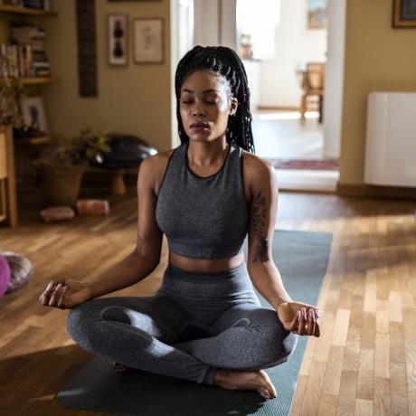 femme noire assise dans une pièce ensoleillée méditant en posture de lotus