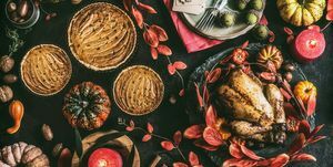 Table de dîner de Thanksgiving avec poulet entier rôti ou petite dinde, tarte à la citrouille sur fond rustique foncé avec assiettes, sauce, couverts, étiquettes de table, bougies allumées, feuilles d'automne rouges, noix et décoration festive, vue de dessus, nature morte, télévision poser