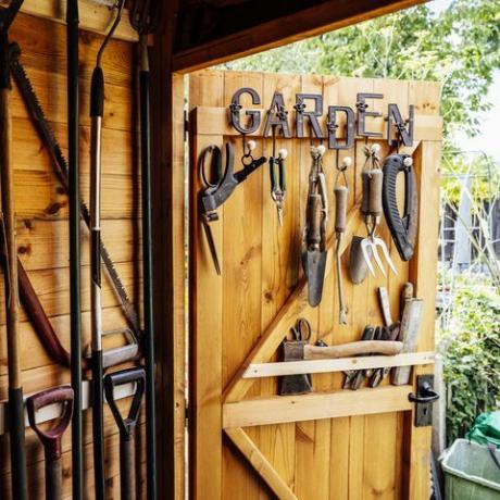 vue intérieure avec porte ouverte d'un hangar organisé rempli de râteau, pelles, taille-bordures, scie et autres outils à main nécessaires à l'entretien d'un jardin bien entretenu