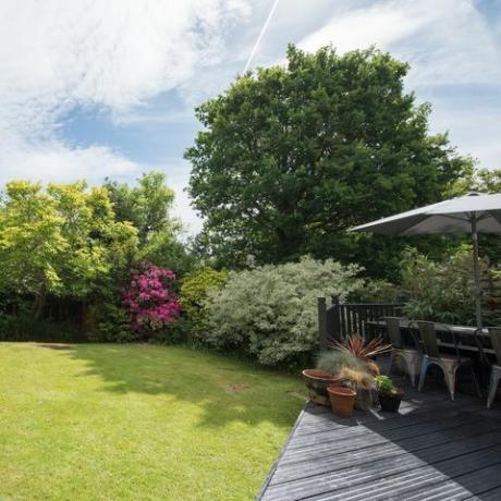 Une vue générale d'un jardin à l'arrière avec une terrasse grise avec table et chaises de jardin lors d'une journée ensoleillée dans une maison